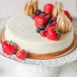 White round delicious cake decorated with blackberries and strawberries on white table in bright kitchen