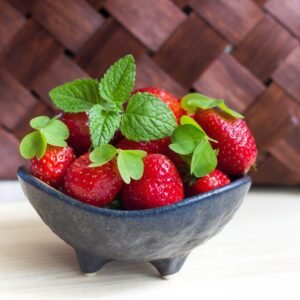 Vibrant fresh strawberries with mint leaves in a black ceramic bowl. Perfect for healthy eating concepts.